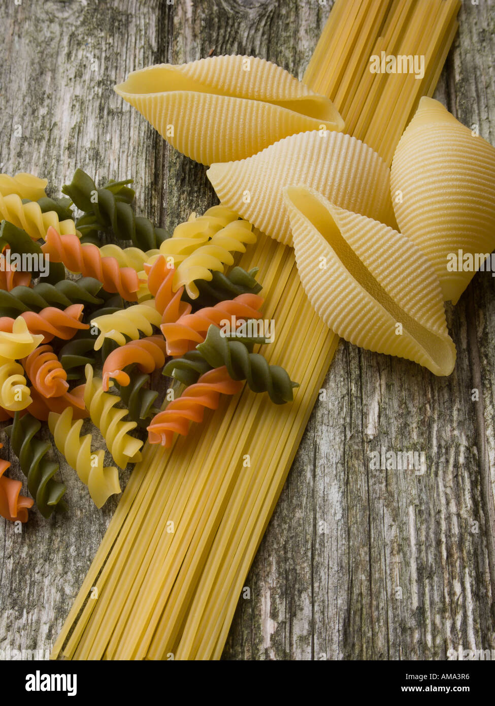 Three types of pasta spaghetti rotelle and conchiglie on a rough wood background Stock Photo