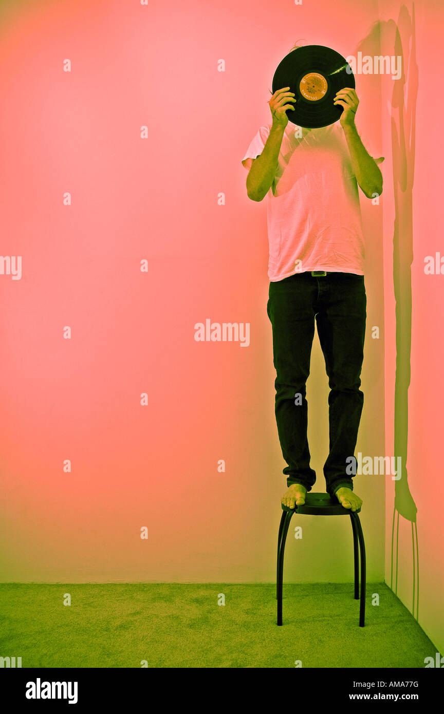 young man in standing on stool in corner holding record in front of his face in front of pink