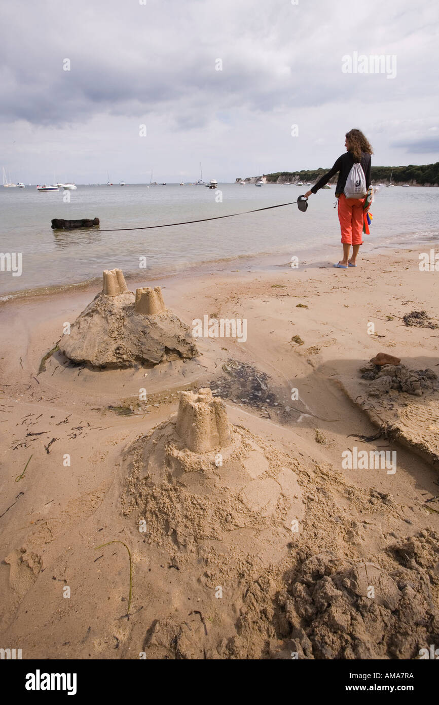 UK Dorset Studland Bay West Beach sandcastles and woman walking dog on long leash Stock Photo