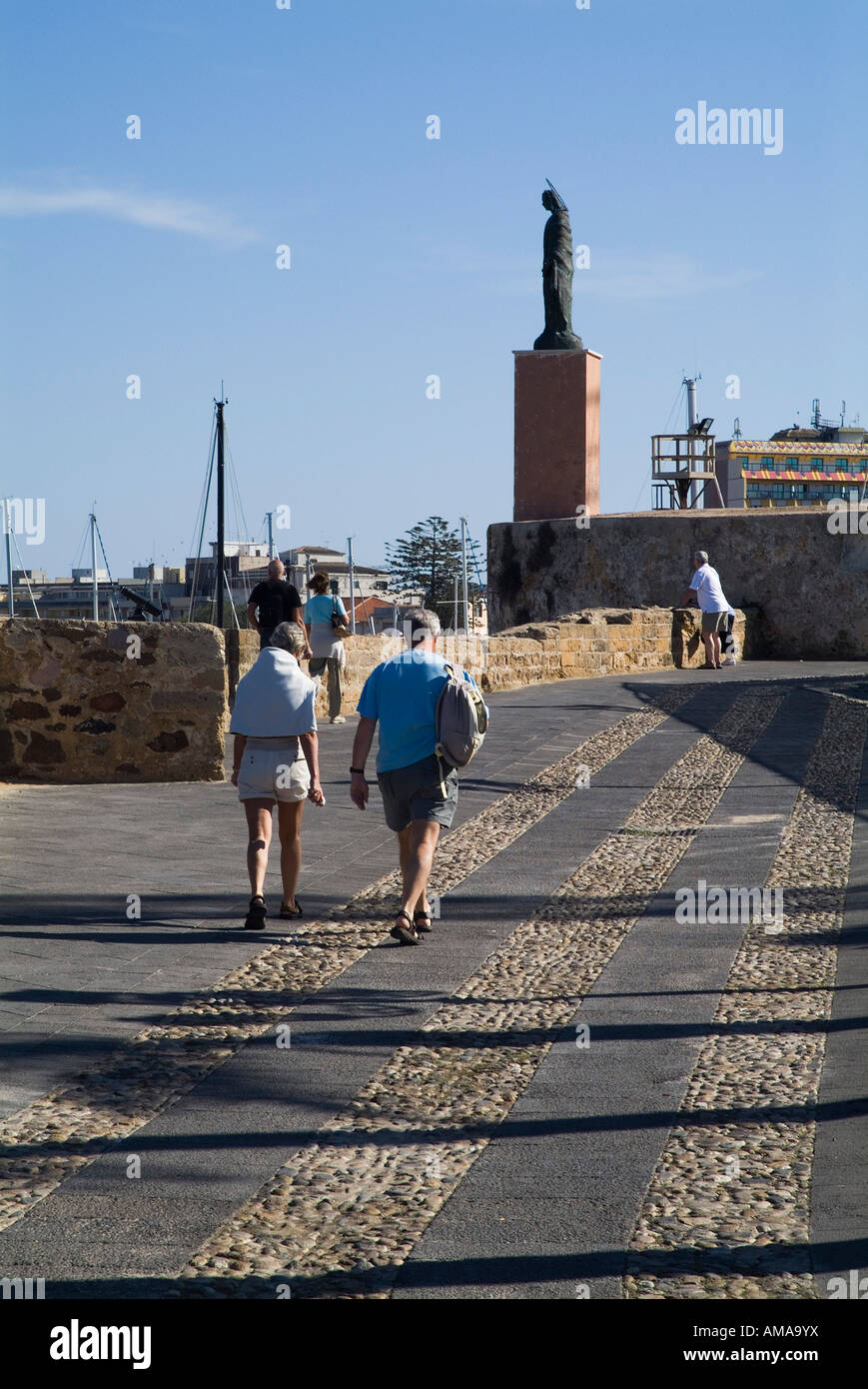 dh St Elmo statue ALGHERO SARDINIA Sant Elmo tourist couple walking along  old city walled promenade Stock Photo - Alamy