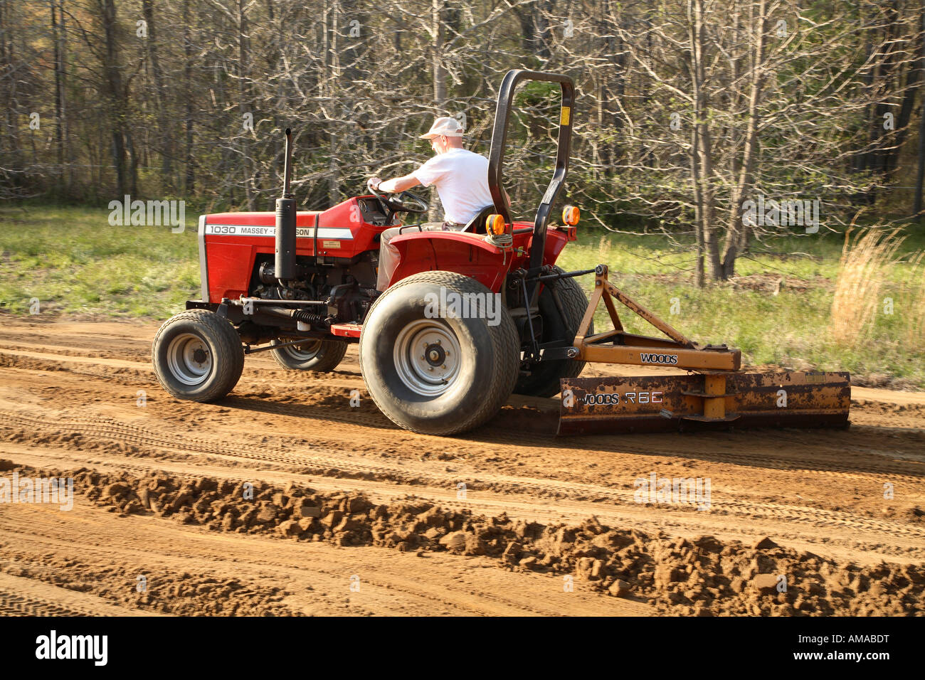 Man driving small tractor and scraping field with grading blade Stock