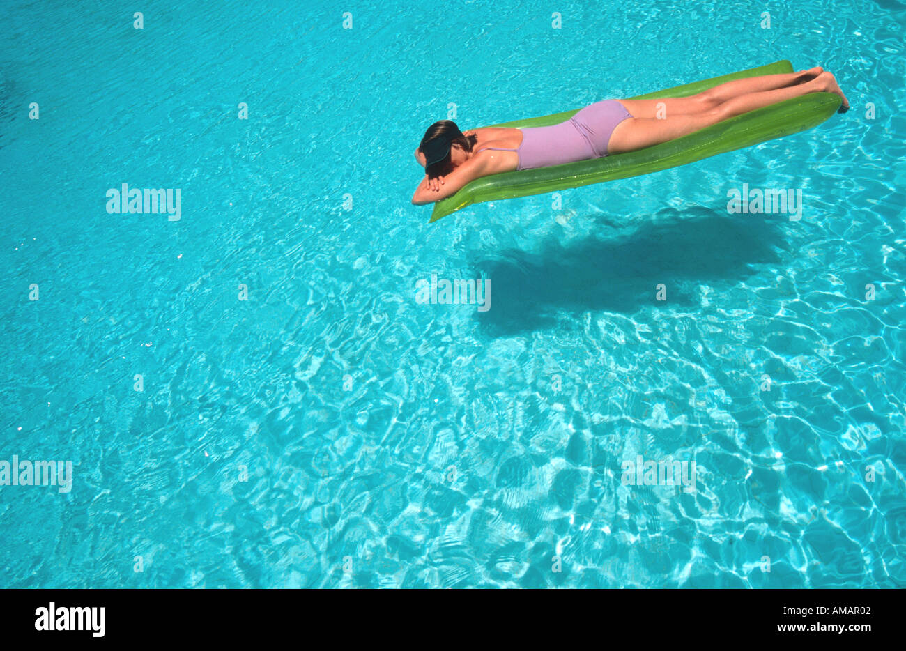 woman female floating on inflatable air bed li lo on water in bright blue swimming pool Stock Photo