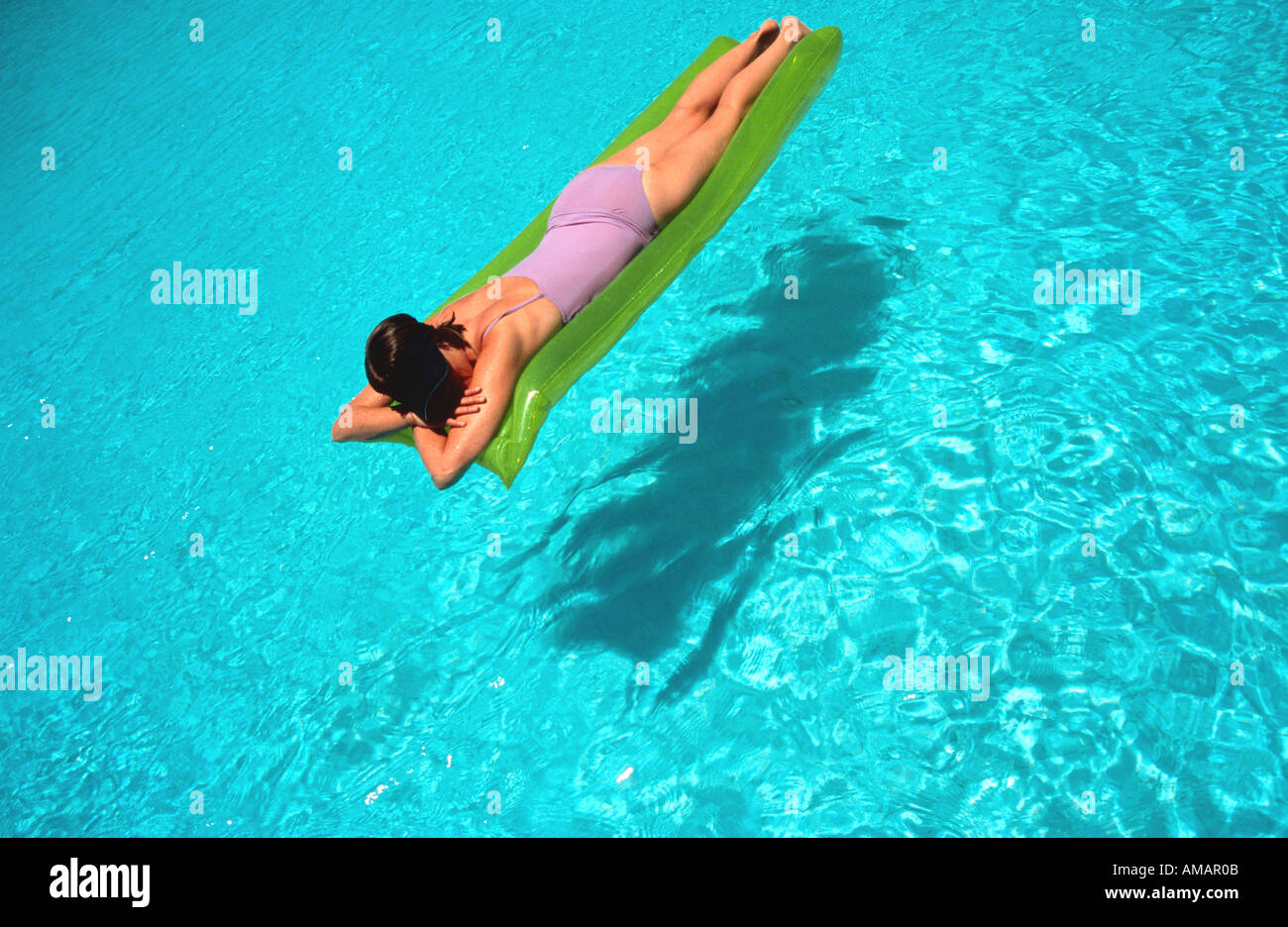 woman female floating on inflatable air bed lilo on water in bright blue swimming pool Stock Photo