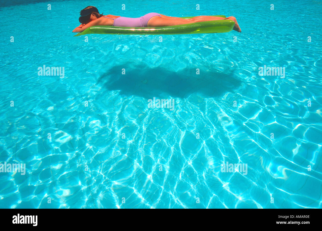 woman female floating on inflatable air bed lilo on water in bright blue swimming pool Stock Photo