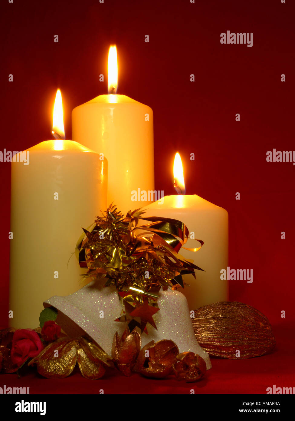 THREE CHURCH CANDLES with Christmas bells and golden cones on dark red background Stock Photo