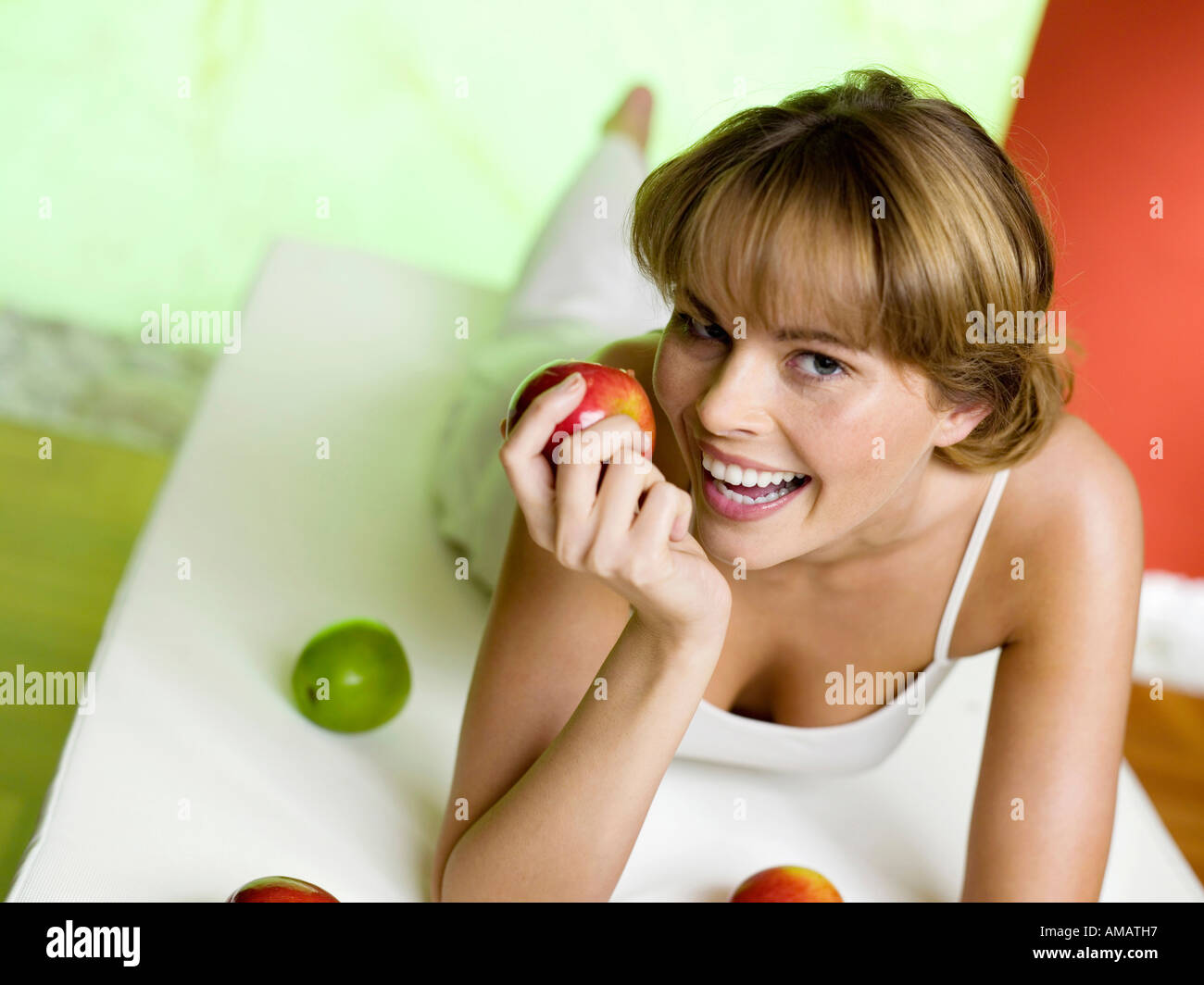 Woman lying on bed with apples, smiling Stock Photo