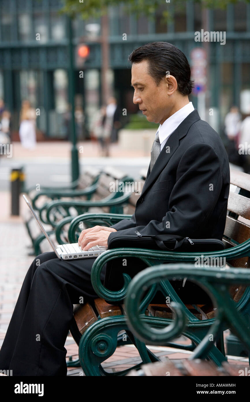 A businessman sitting on a bench and using his laptop Stock Photo - Alamy