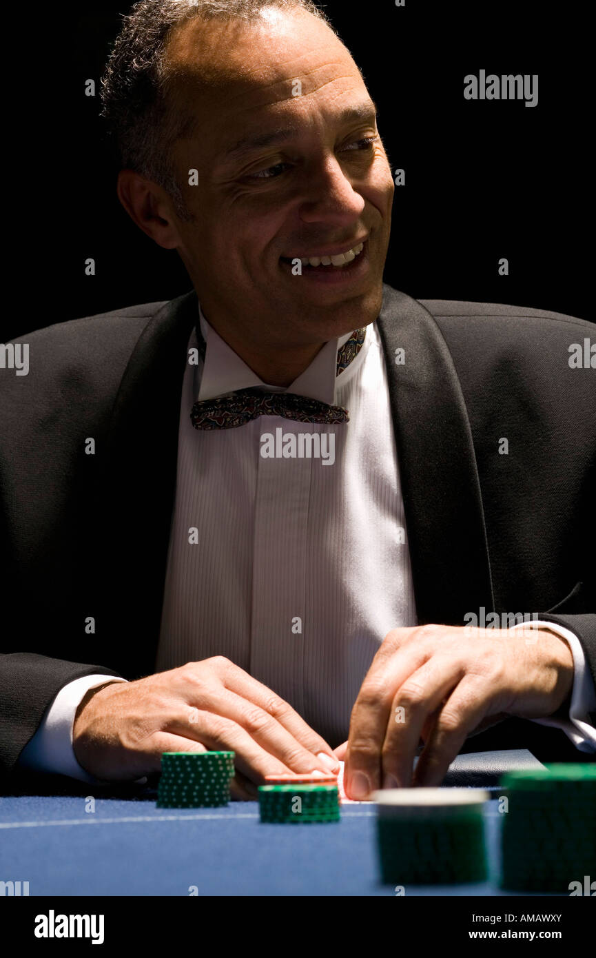 Well dressed man smiling while playing cards at casino table Stock Photo