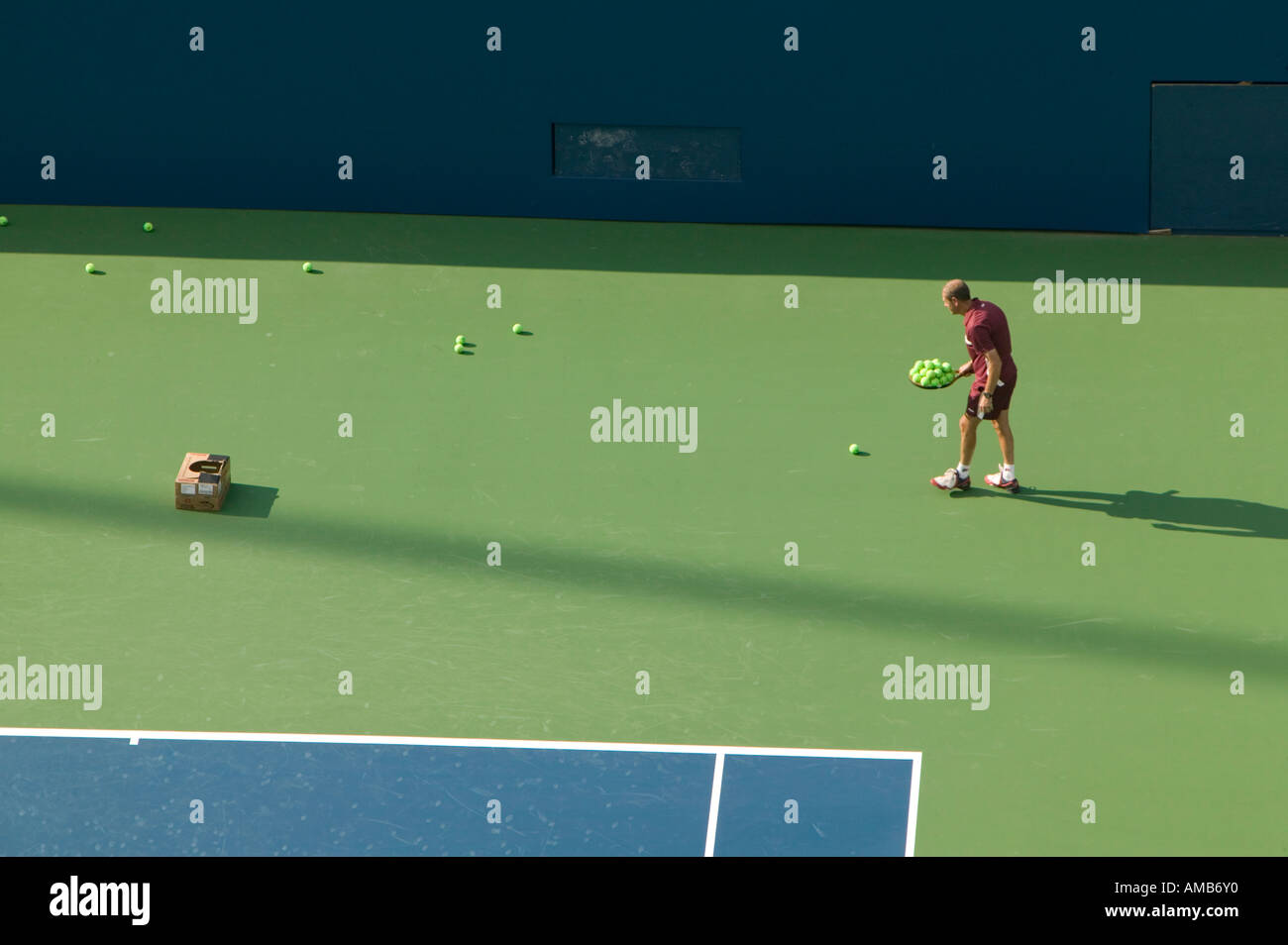 A single tennisman collects yellow tennis balls with his racket during a practice game on a green and blue court August 2005 Stock Photo