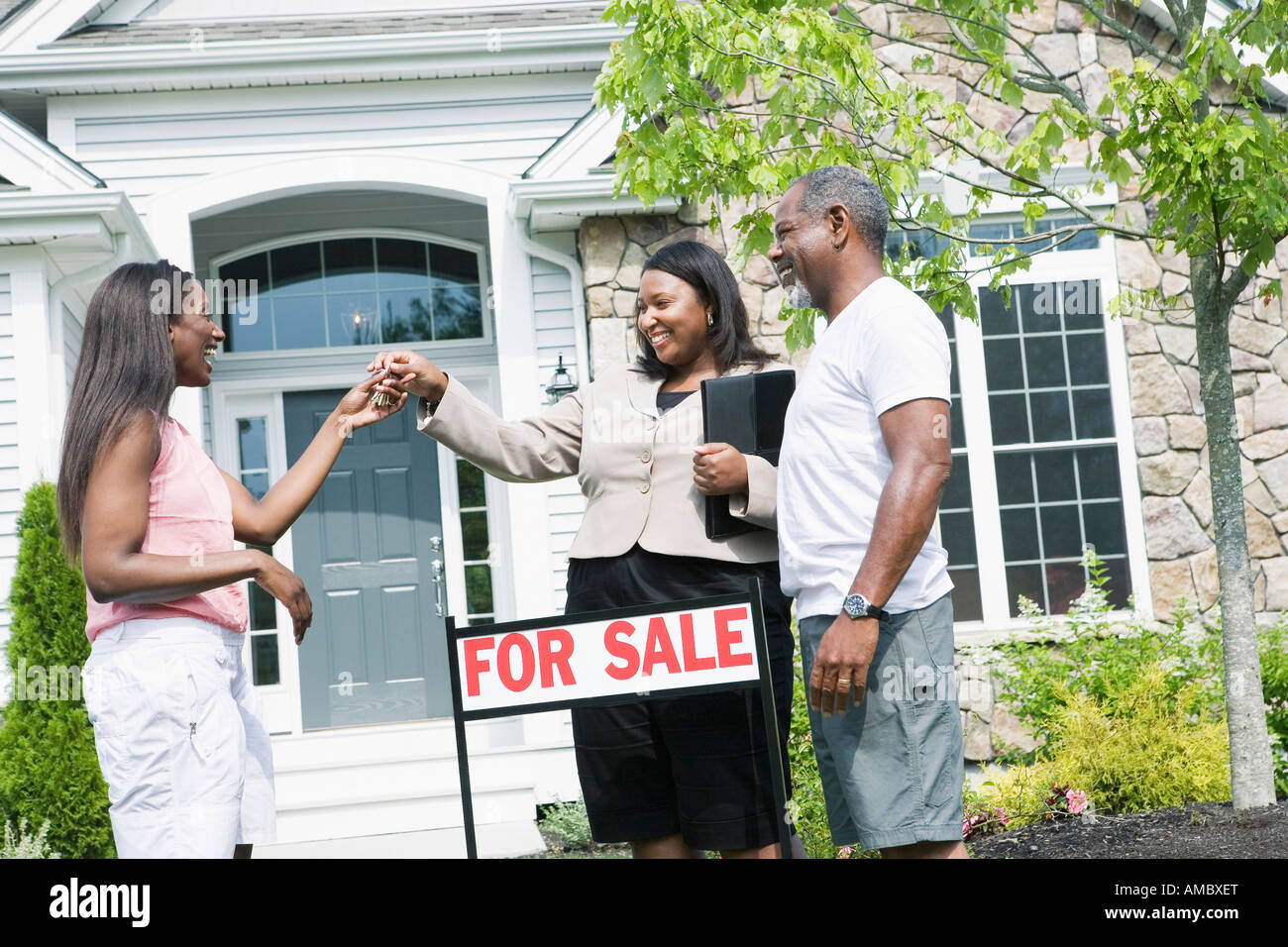 Real estate agent giving key to a middle-aged woman in front of a house ...