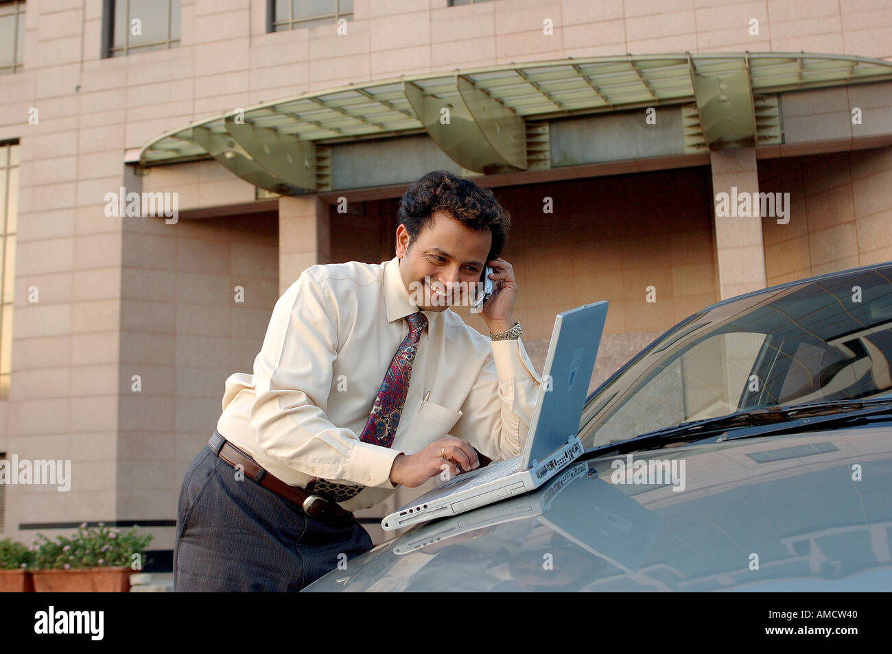 VEP72165 Young Indian Executive with tie smiling and talking on mobile phone and working on computer Stock Photo