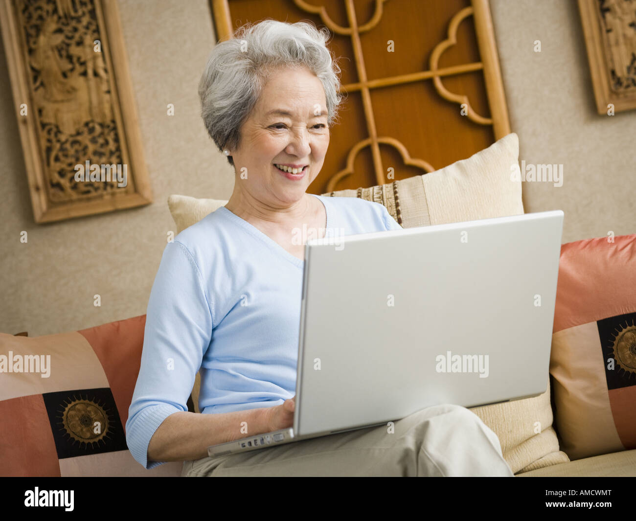 Woman sitting on sofa with laptop smiling Stock Photo