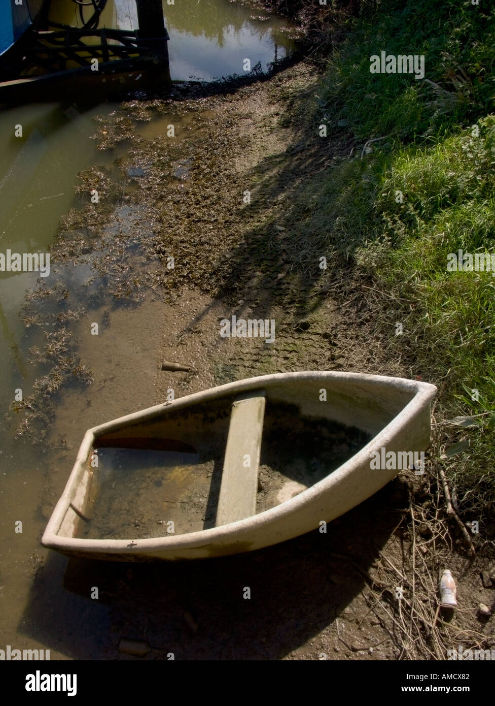 A lone rowing boat beached on mud by a riverbank Stock Photo