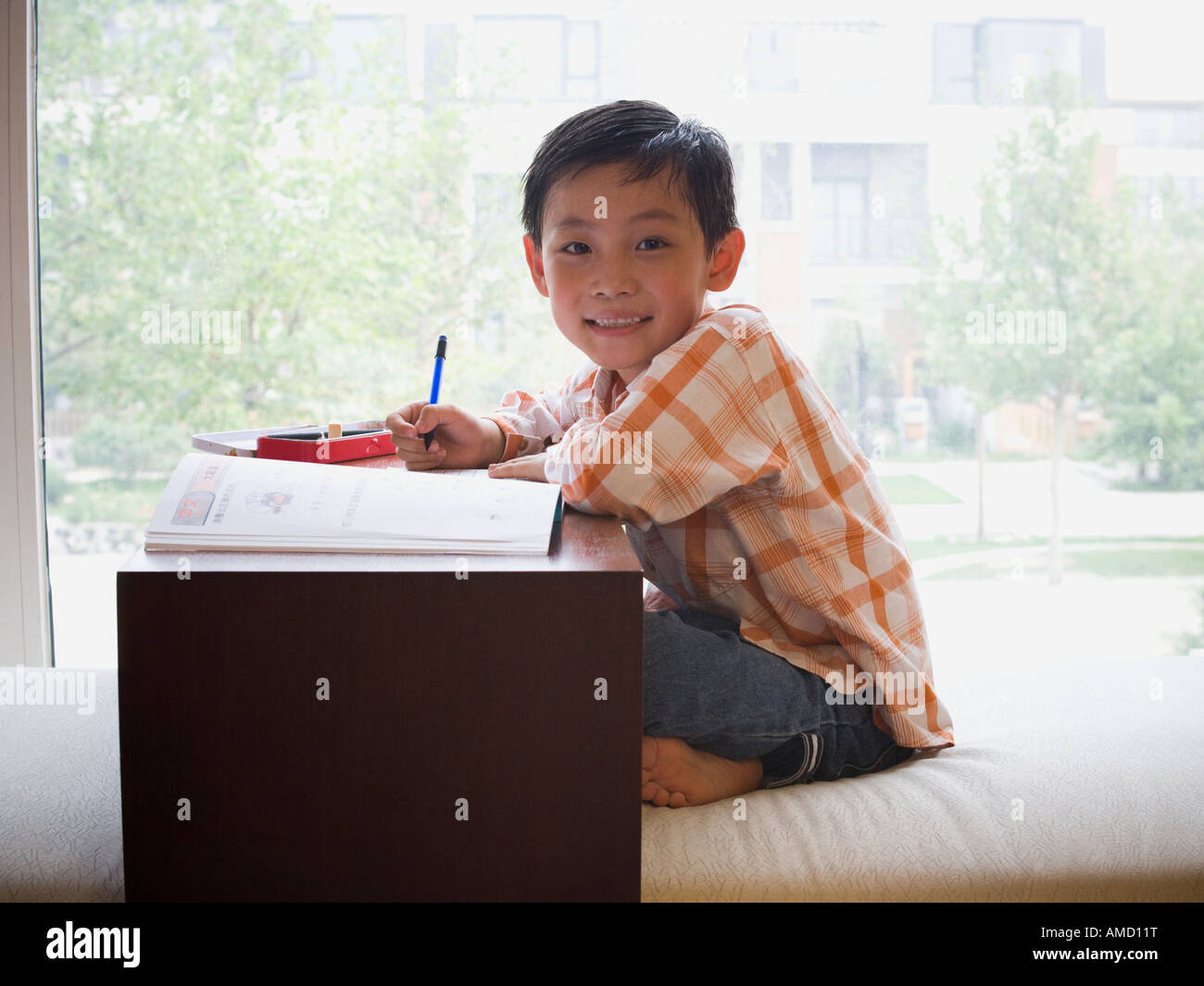 Boy sitting with workbook in front of large window smiling Stock Photo ...