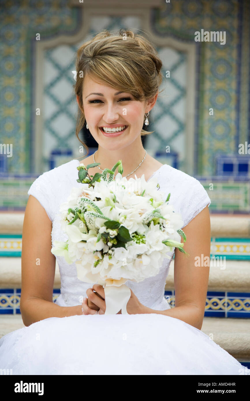Bride sitting on steps with bouquet smiling Stock Photo - Alamy