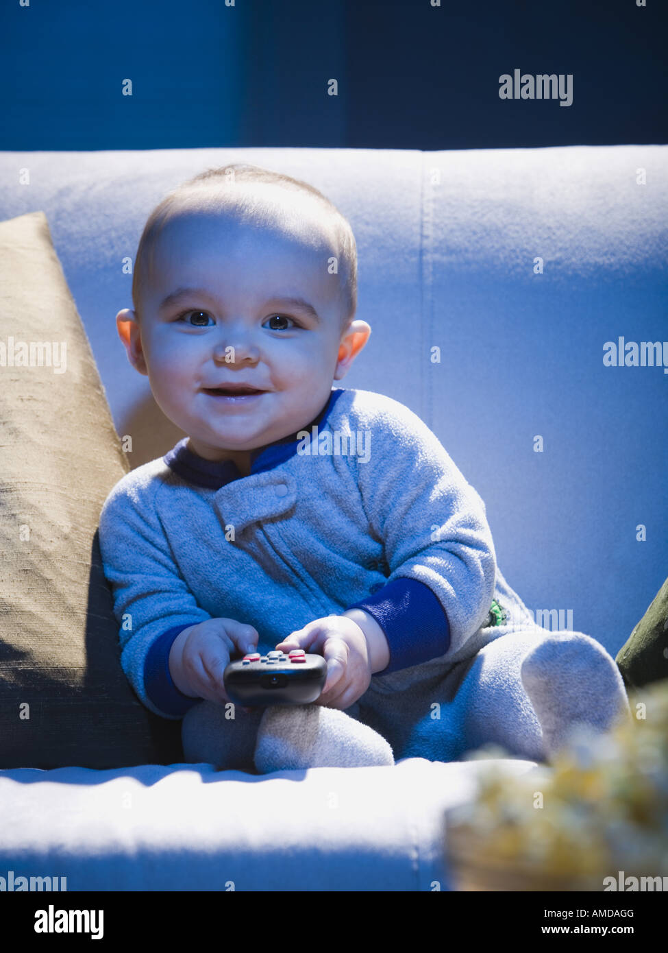 Baby on sofa with television remote smiling Stock Photo