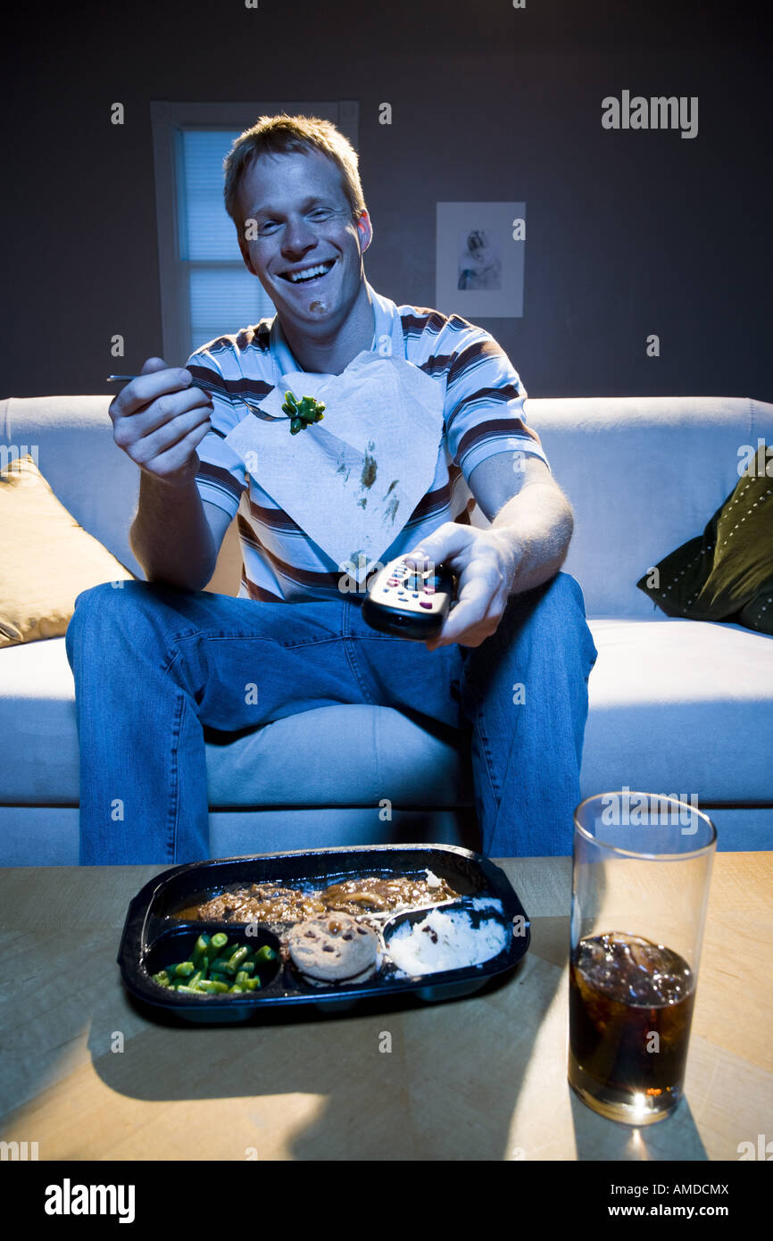 Man on sofa with frozen dinner and napkin with food smiling Stock Photo