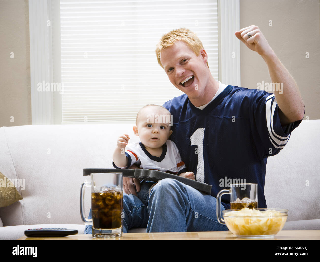 Man and baby on sofa cheering Stock Photo