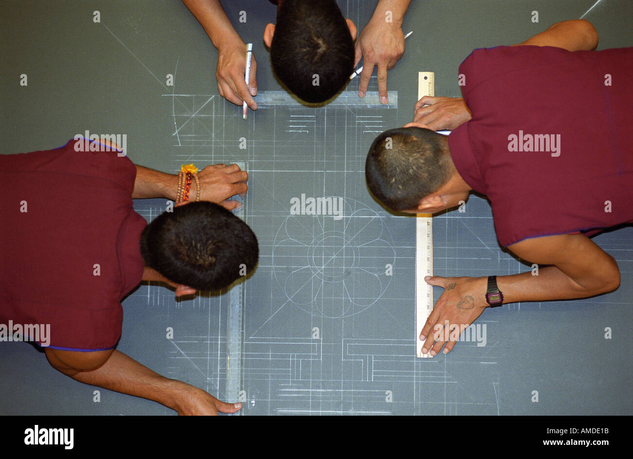 Three monks draw chalk line designs as the first stage of the mandala creation Stock Photo