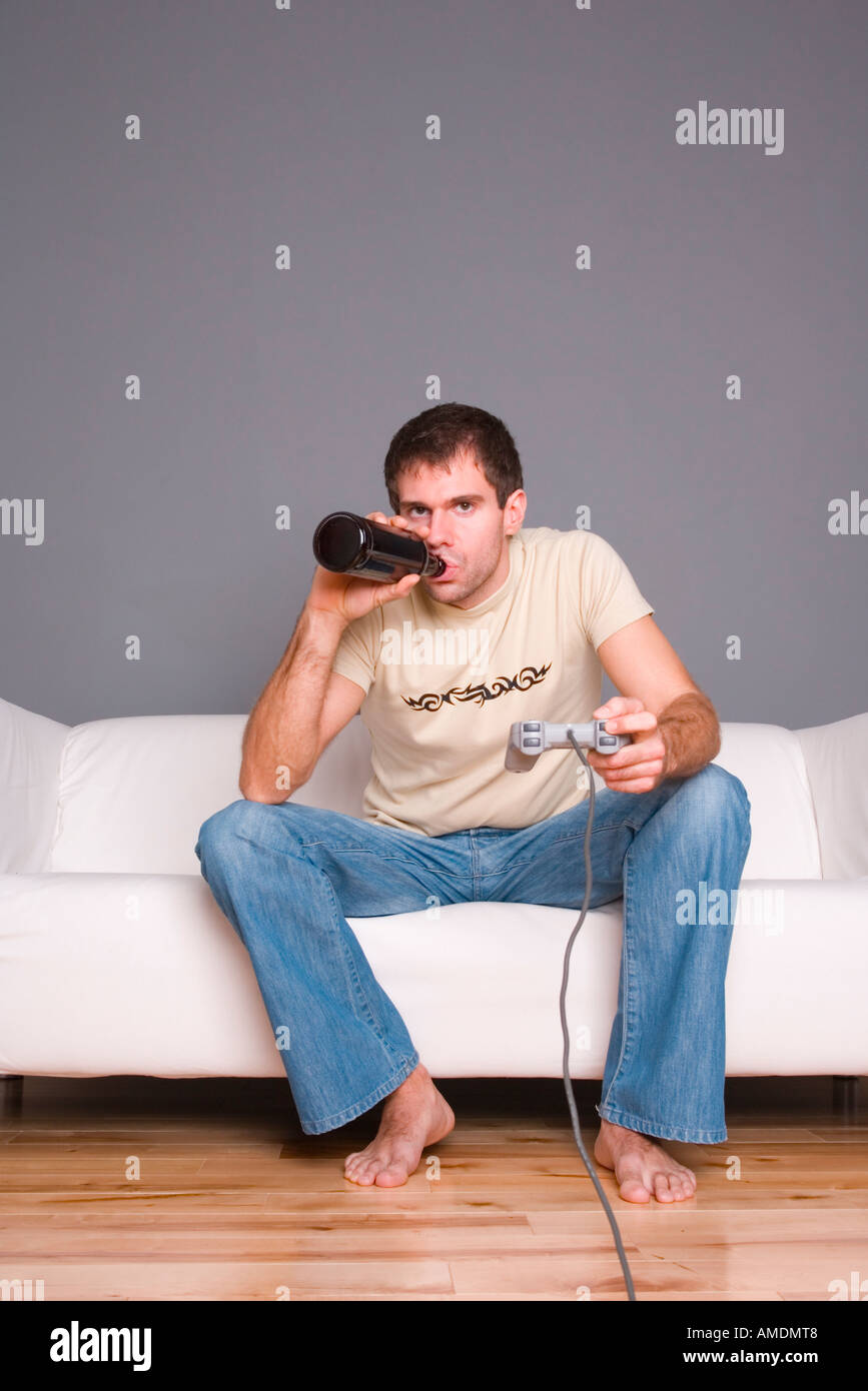 Man playing games console whilst drinking from a brown bottle Stock Photo
