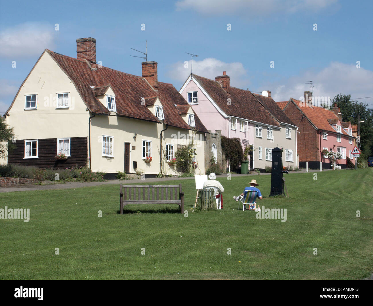 Monks Eleigh village green cottage homes back view people relaxing  artist & easel at work historical old water pump Suffolk East Anglia England UK Stock Photo