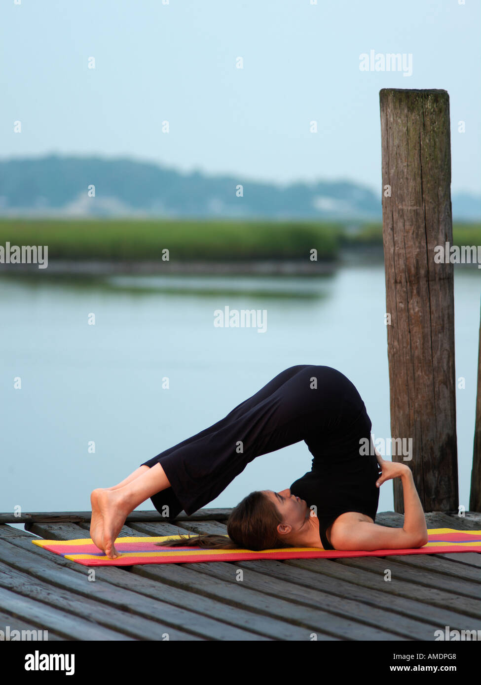 Woman doing yoga plow position early morning on dock Virginia Beach VA Stock Photo