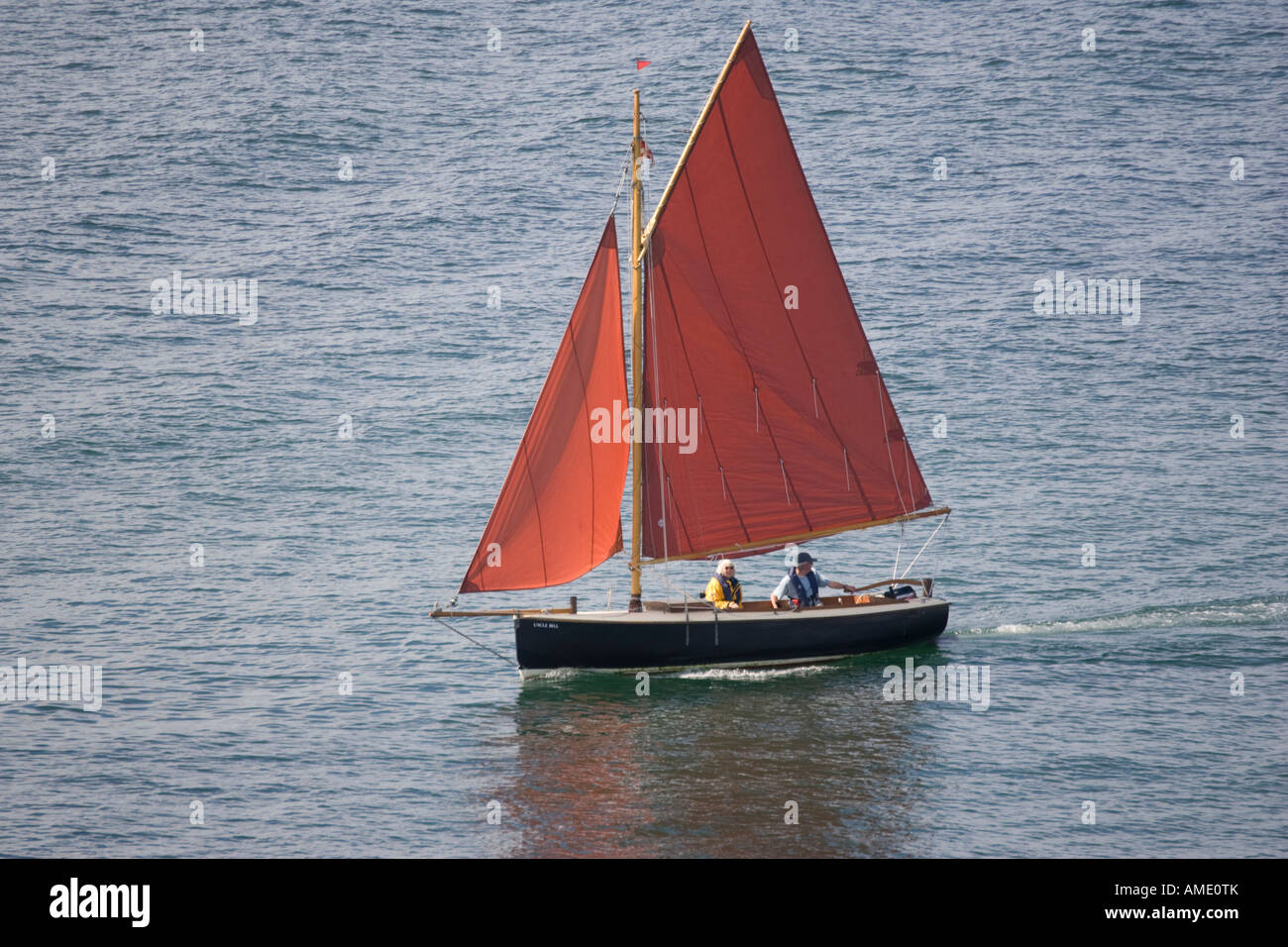 Small gaff rigged sailing boat with orange sails Poole Harbour Dorset UK Stock Photo