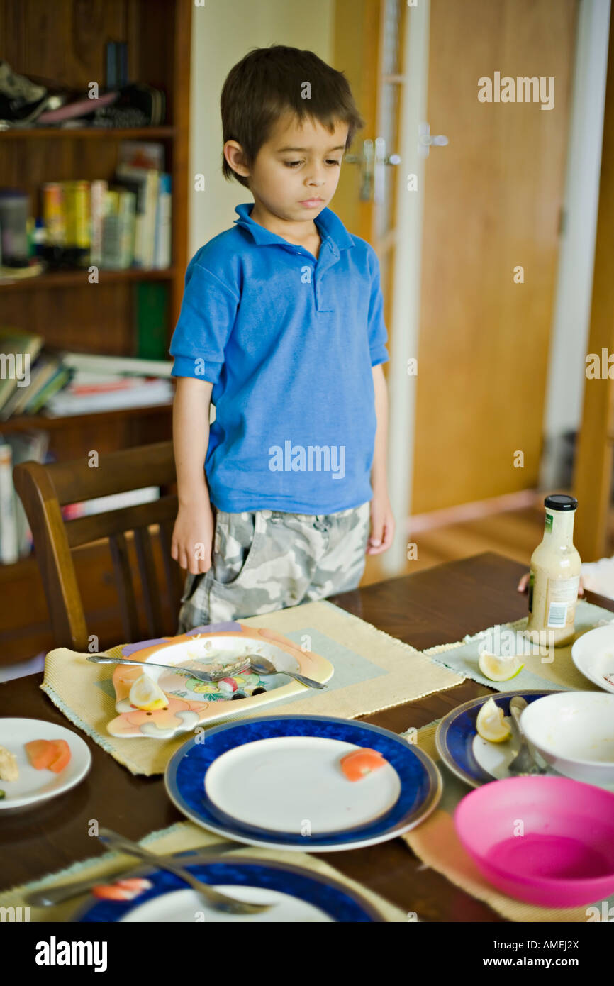 Boy looks at dining table with empty plates after lunch Stock Photo