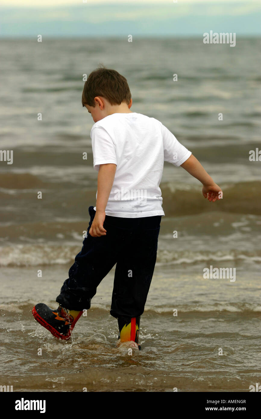 sixyearold boy paddling in the sea whilst wearing Wellington boots Stock Photo Alamy