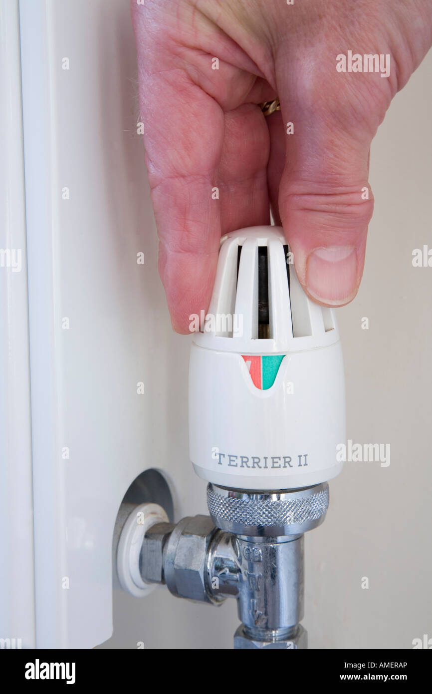 Person's hand turning down household heating radiator thermostat