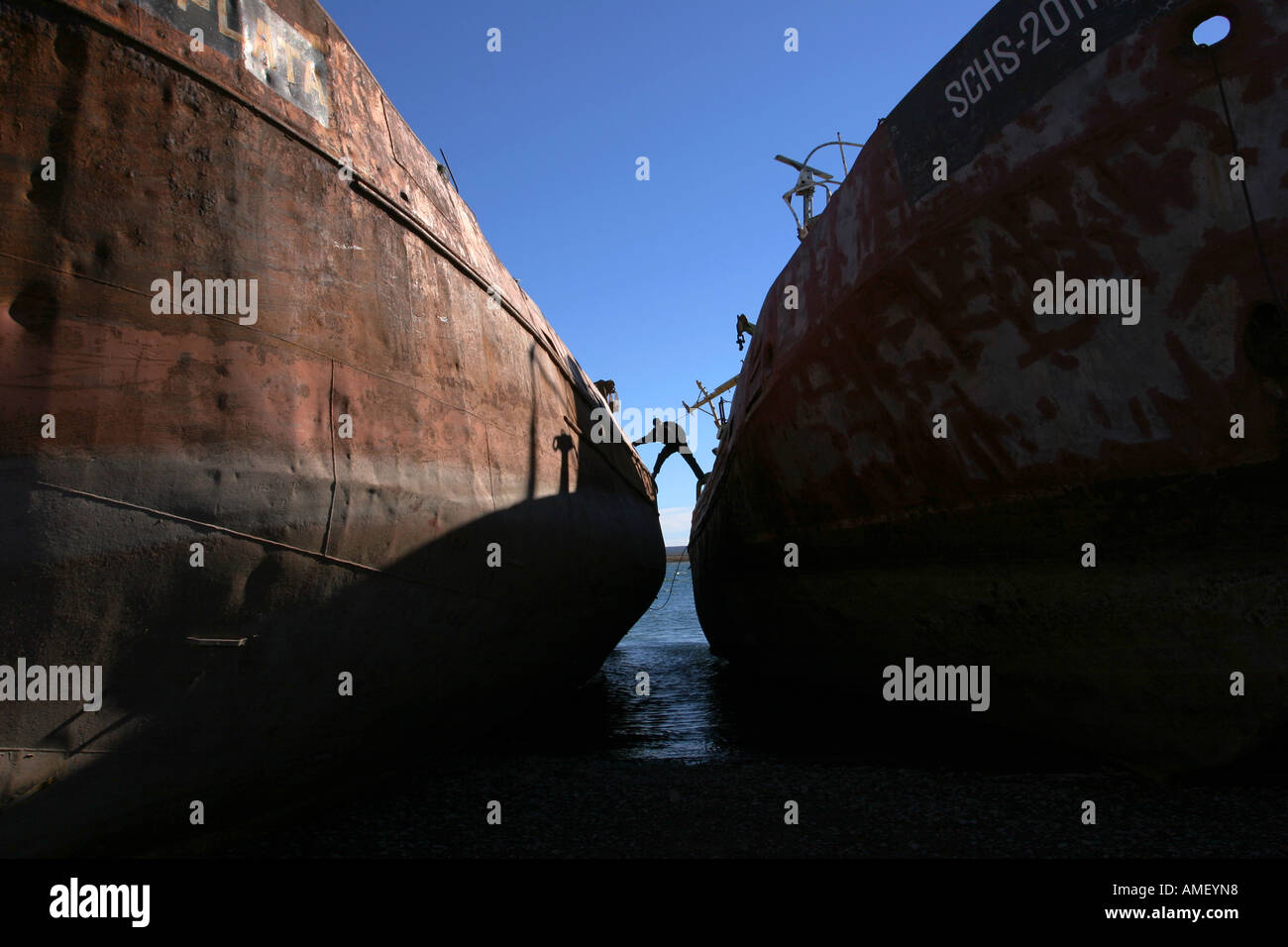 A man going from one ship to another in Mar del Plata, Argentina. The fishing boat hull looks old, oxidize and rusty, corroded b Stock Photo