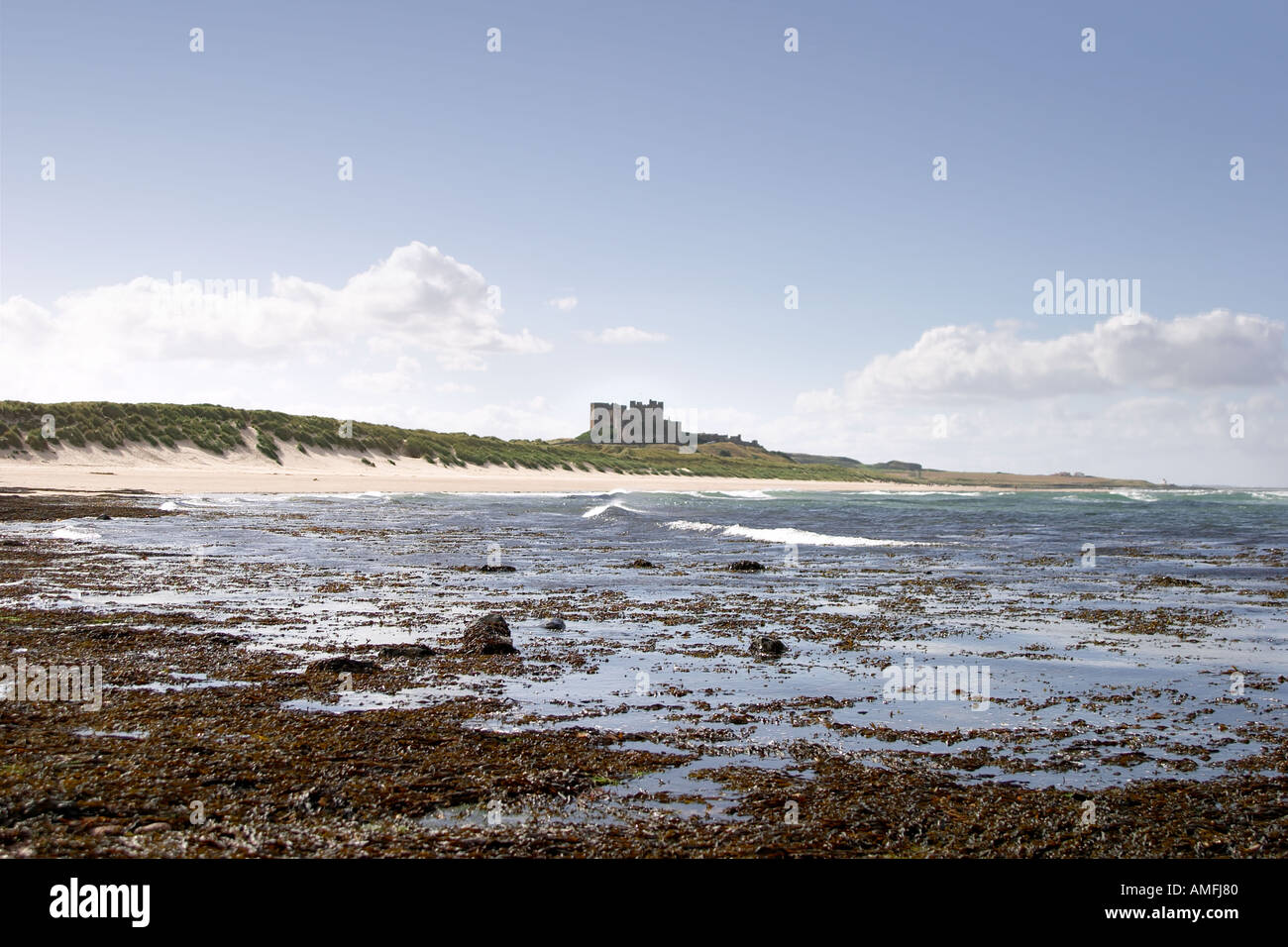 landscape shot of Bamburgh castle as taken from the beach showing sand sea and sky Stock Photo