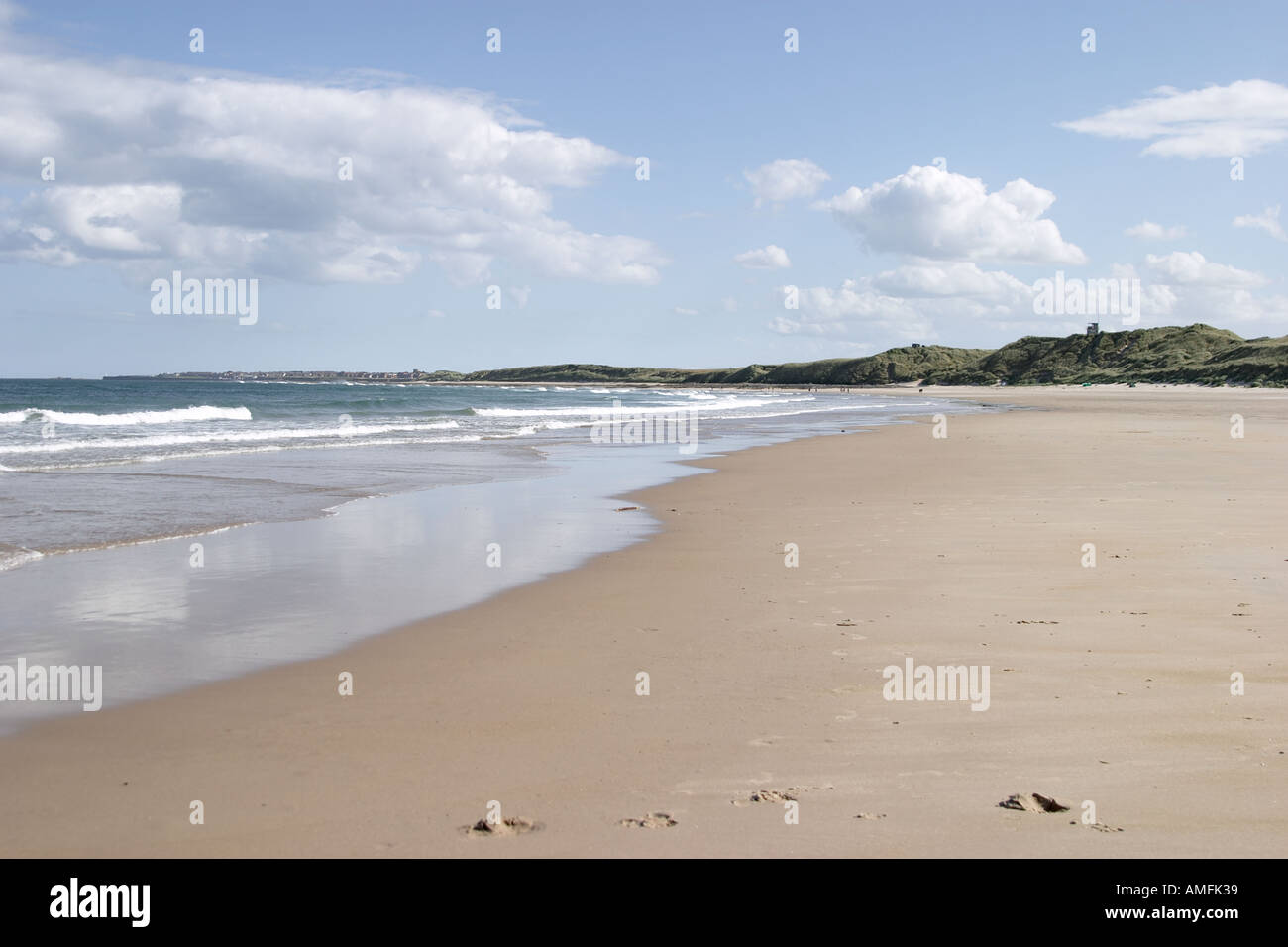 landscape shot showing large expanse of sandy beach with tide coming in Blue sky with white clouds and sand dunes Stock Photo