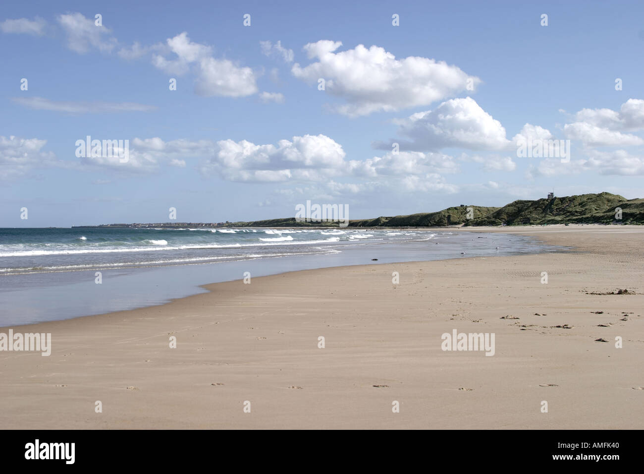landscape shot showing large expanse of sandy beach with tide coming in Blue sky with white clouds and sand dunes Stock Photo