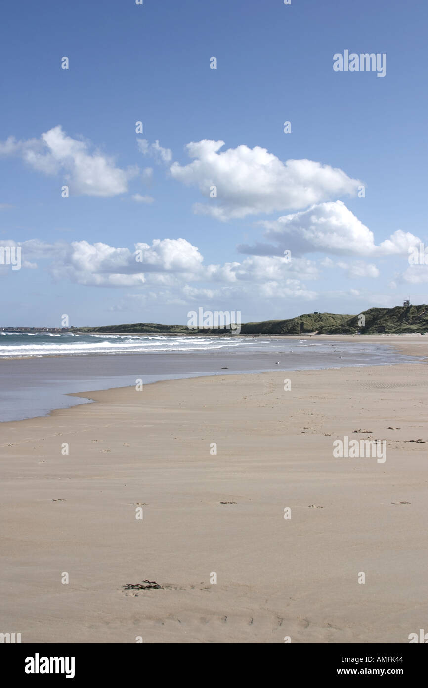 portrait shot showing large expanse of sandy beach with tide coming in Blue sky with white clouds and sand dunes Stock Photo