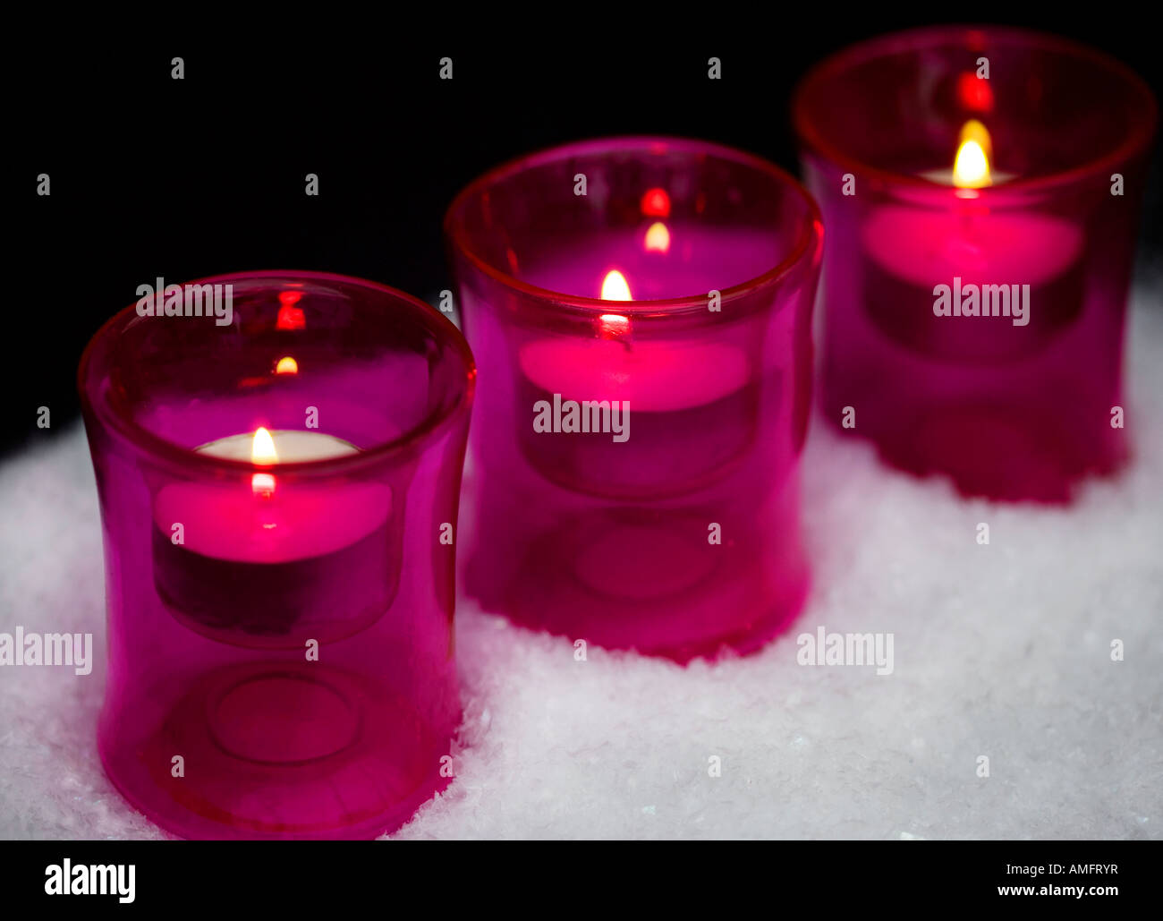 Candles in pink glass tealight holders shot standing in faux snow with
