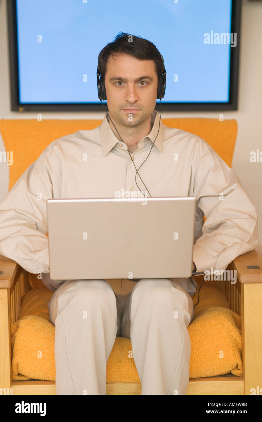 Man using a laptop with plasma screen in background Stock Photo