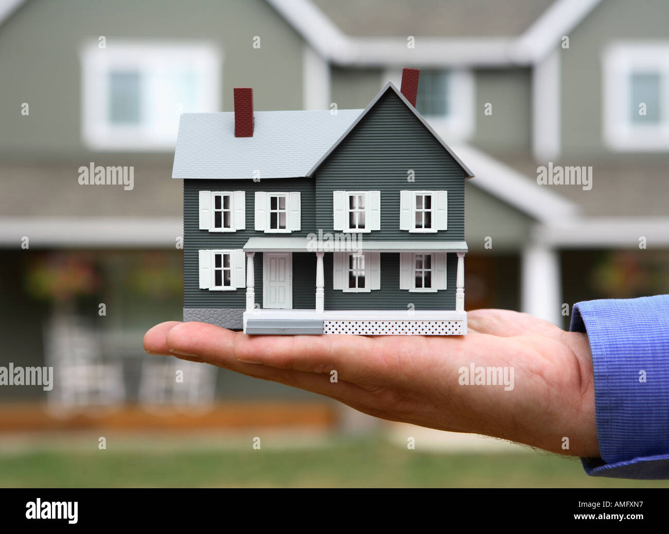 Hand Holding Model House in front of Full Size Home Stock Photo