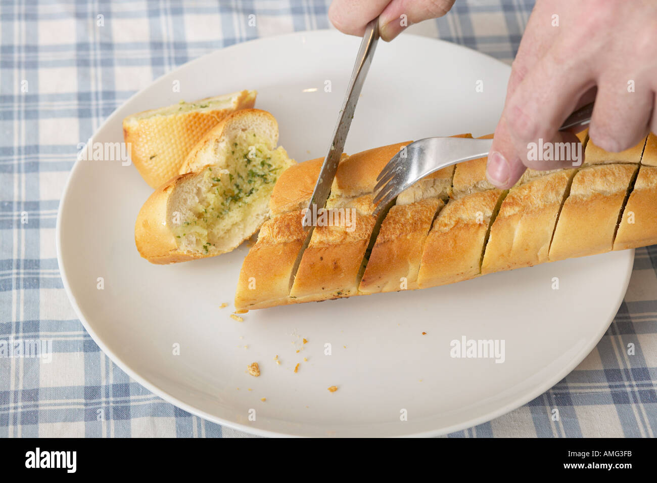 hand cutting slice of garlic bread with knife Stock Photo