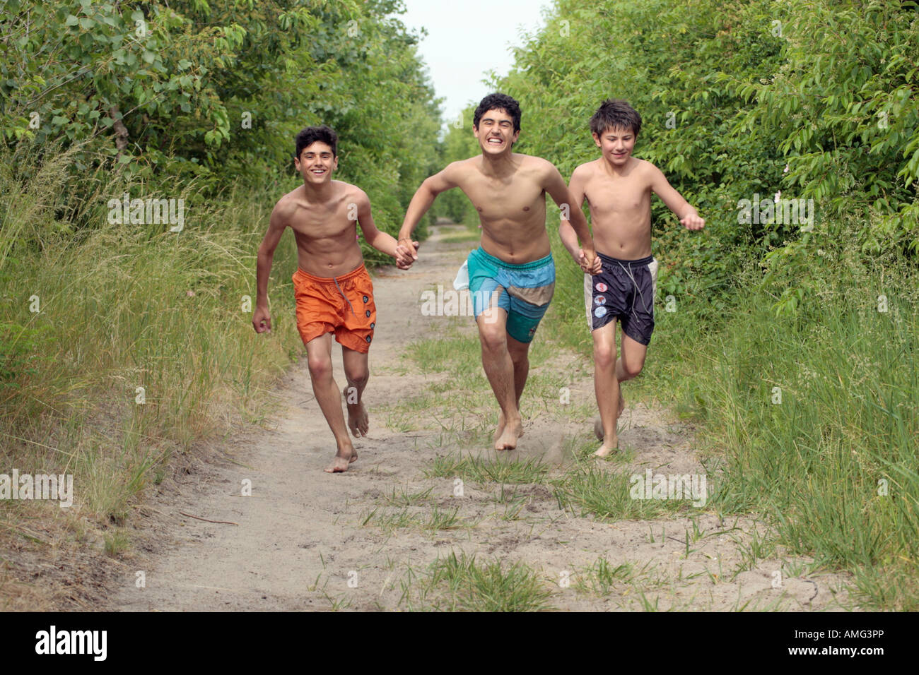 three teenage boys running along a country lane in their bare feet Stock Ph...
