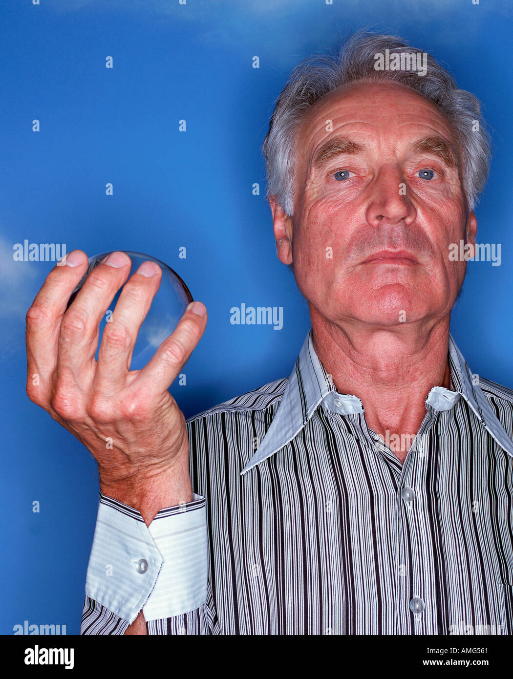 A portrait of a mature man wearing shirt holding a crystal ball against a blue sky background Stock Photo