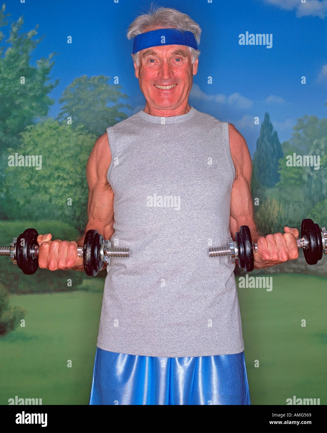 A portrait of a mature man in vest holding dumbells against a garden background Stock Photo