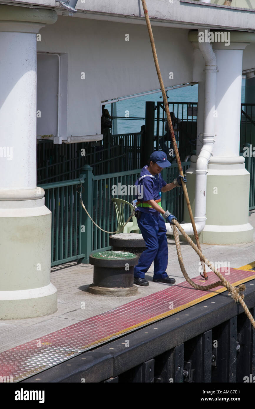 A sailor on one the Kowloon side pier of the Star Ferry prepares to throw a mooring rope to a colleague on a ferry as it leaves Stock Photo