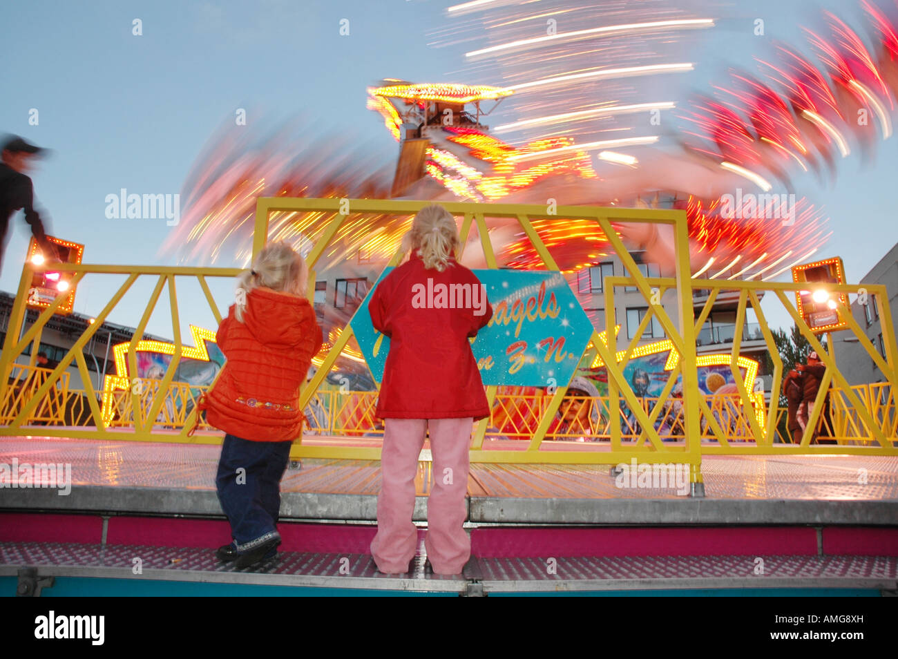 two toddlers in red coats watching fairground attraction from behind ...