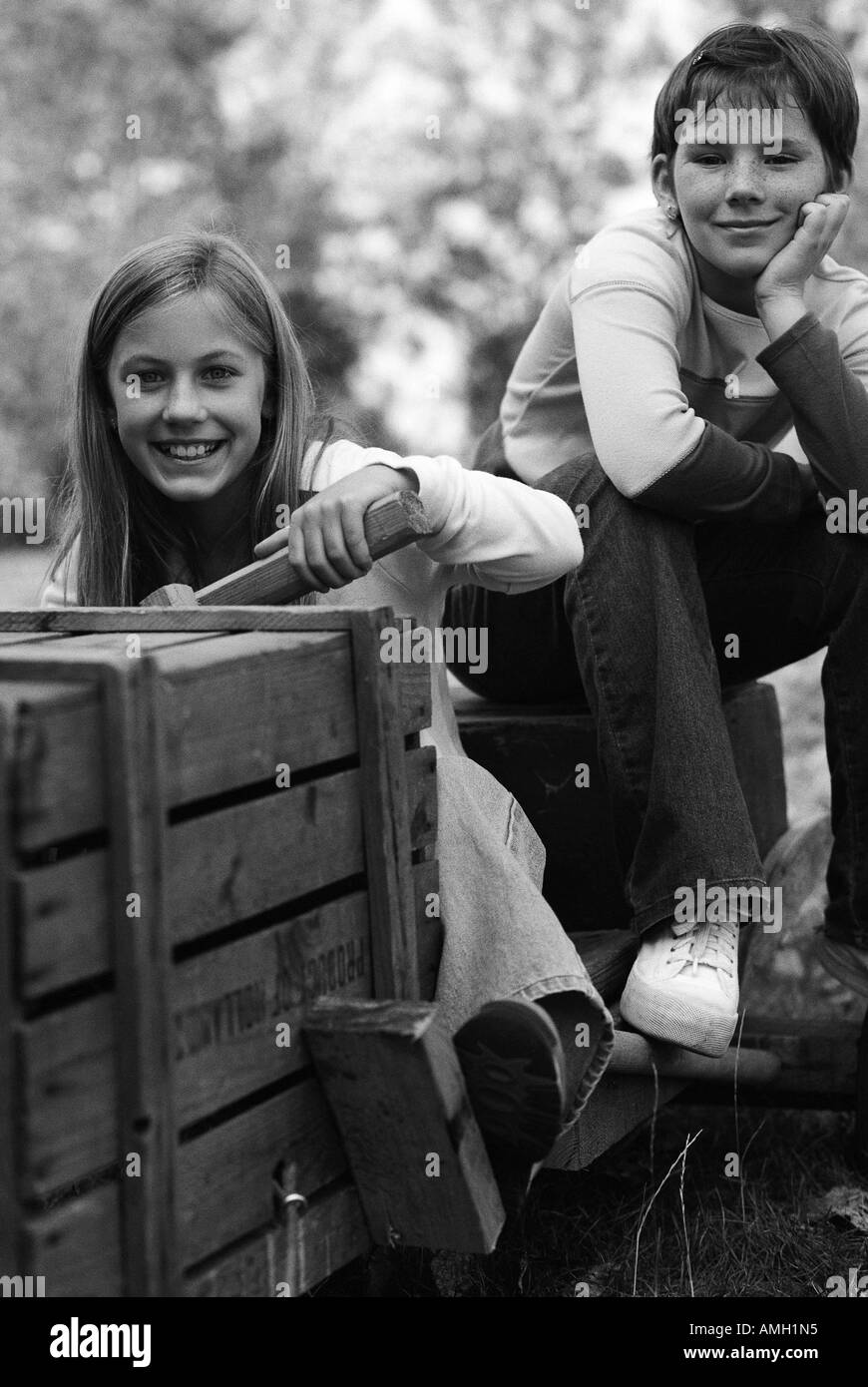 Portrait of Two Girls Sitting On Soapbox Car Outdoors Stock Photo