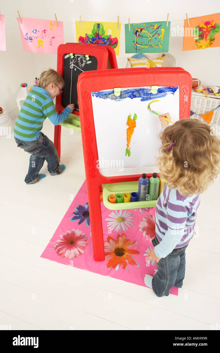 Two children paint at an easel and draw on a chalk board Stock Photo