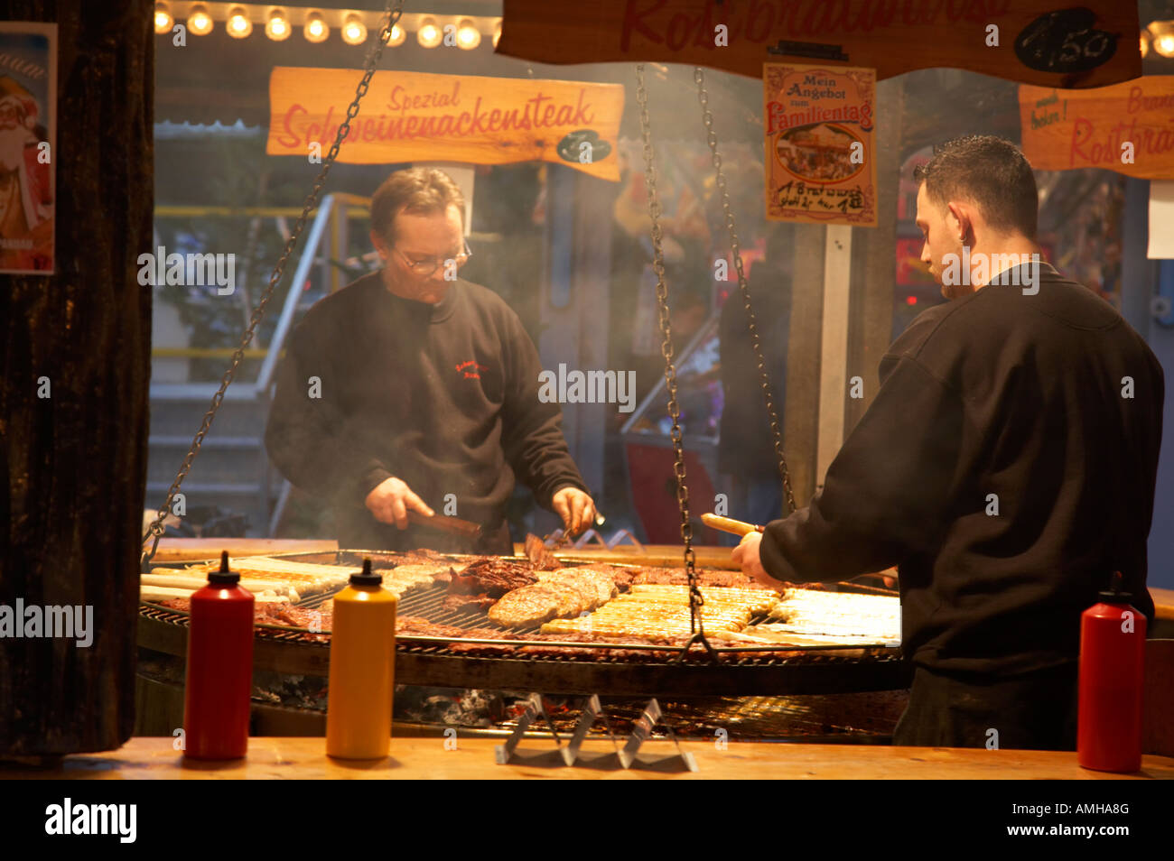 Two men on a fast food meat selling stall cook rostbratwurst and steak on a huge open grill spandau christmas market Berlin Stock Photo