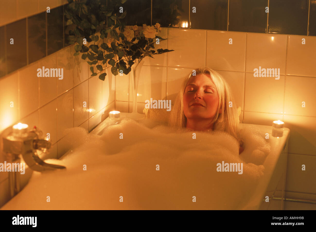 Candle lit bubble bath for relaxed blond woman Stock Photo