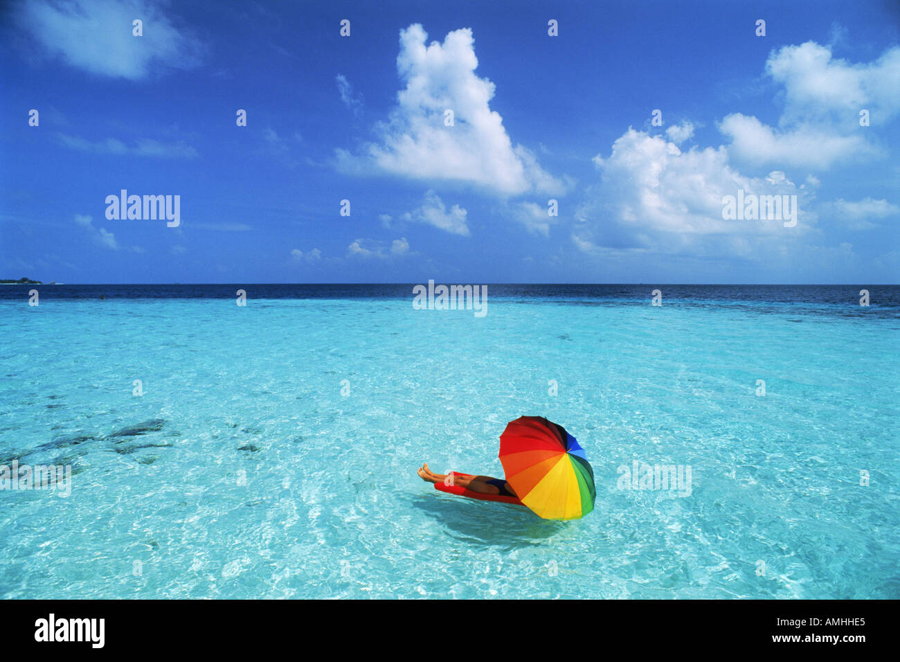 Spending dream holidays on air mattress under colorful parasol between blue skies and waters in aqua paradise Stock Photo
