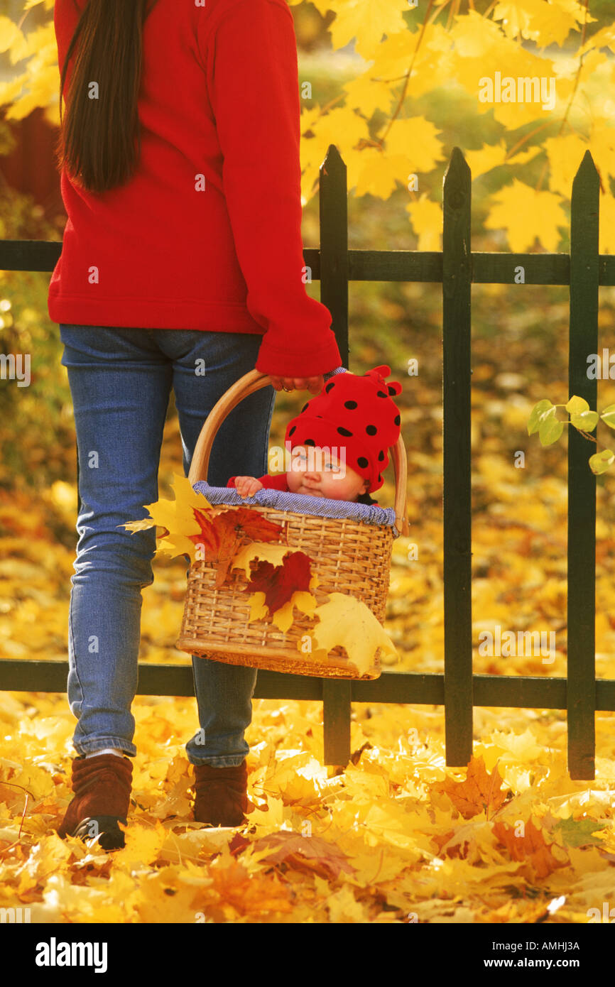 Mother carrying baby in basket amid autumn colors Stock Photo